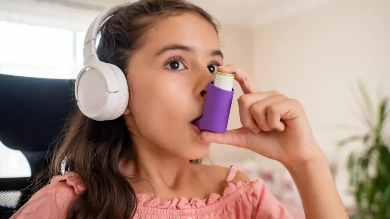 Mädchen mit Kopfhörern benutzt Inhalator gegen Asthma durch Stress.