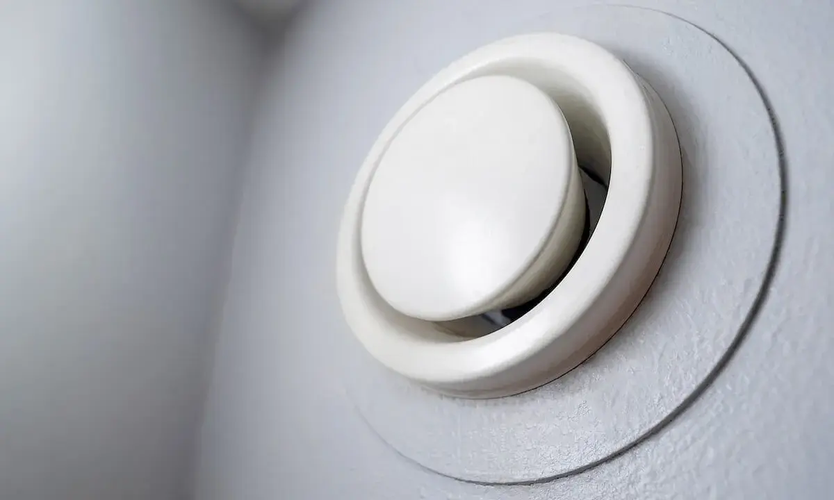 Grille de ventilation blanche, ronde et réglable, fixée sur un mur gris. Un système vmr hygroréglable pour une meilleure qualité de l'air.