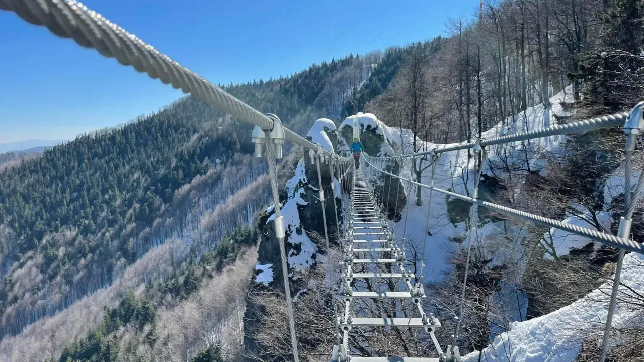 Zimowa przygoda na wiszącym moście nad przepaścią. Skalka pri Kremnici w śnieżnej odsłonie, z widokiem na zalesione zbocza.