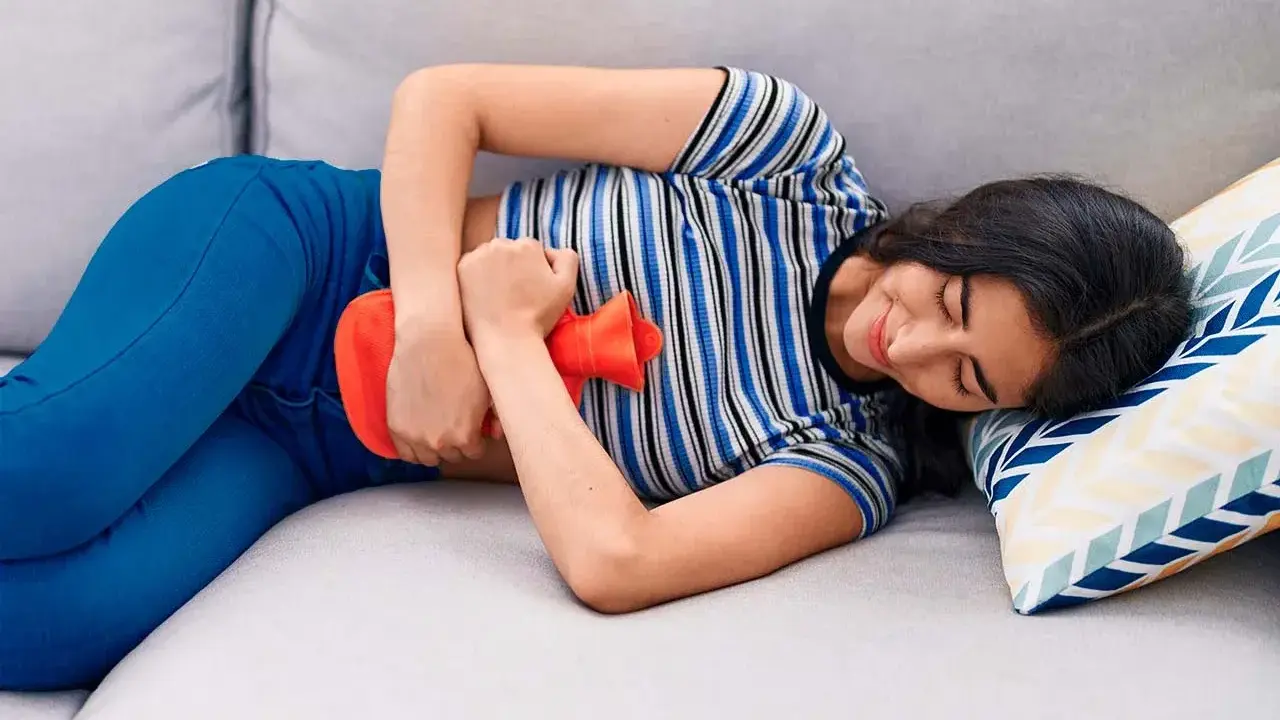 Joven con bolsa de agua caliente en el abdomen, aliviando el dolor de cólicos.