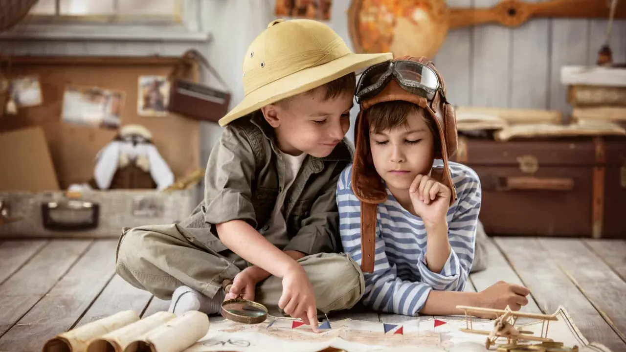 Dos niños planean una aventura en una casa rural para niños, con un mapa, lupa y sombrero de explorador.