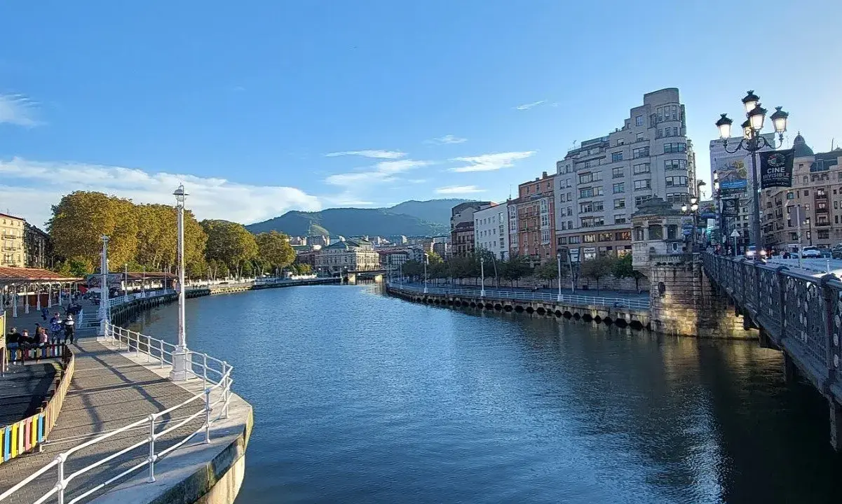 Blick auf den Bilbao Fluss mit Gebäuden und einer Brücke im Hintergrund.