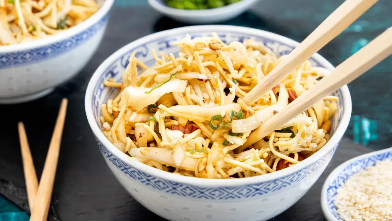 Friss dich dumm Salat: Nudeln, Gemüse und Nüsse in einer Schüssel, bereit zum Genießen mit Stäbchen.