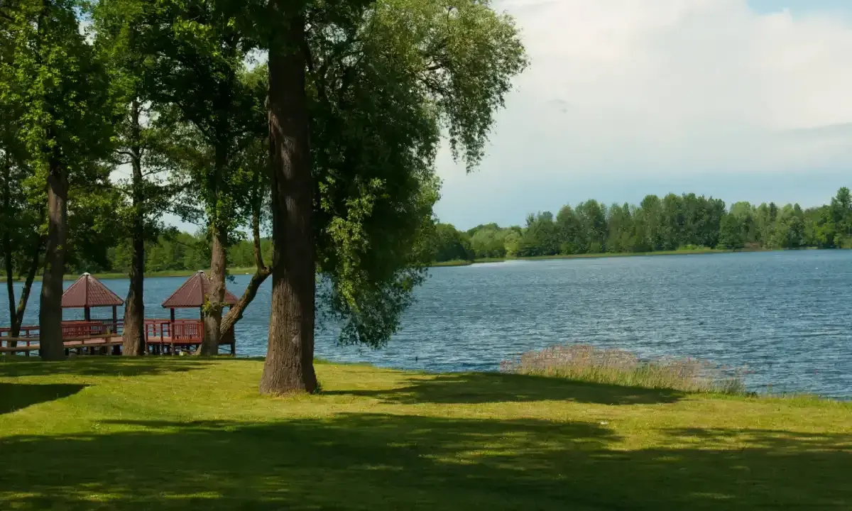 Malownicze jezioro Grabowo z altanami na pomoście, otoczone zielenią i drzewami.