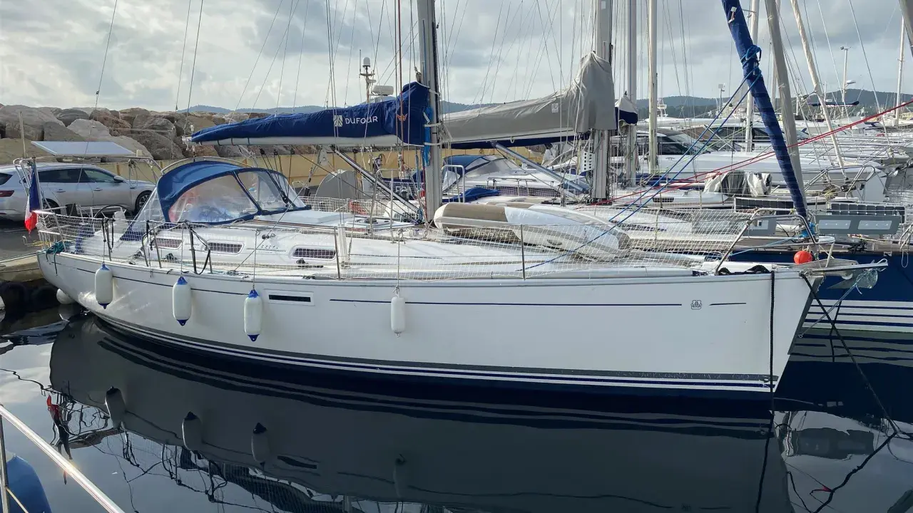 Un voilier Dufour 385 Grand Large blanc, amarré dans un port, reflète son élégance sur l'eau calme.
