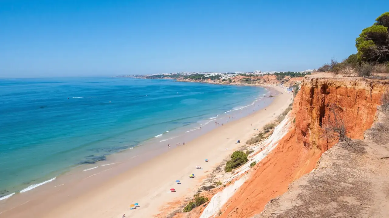 Blick auf den Strand Praia da Falésia mit seinen roten Felsen und der Stadt im Hintergrund.