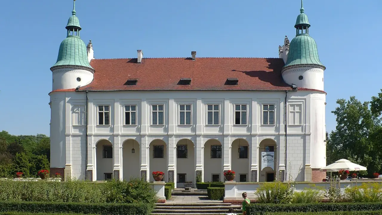 Baranów Sandomierski atrakcje: Zamek z arkadowym podcieniem i zielonymi wieżyczkami, otoczony zadbanym ogrodem.