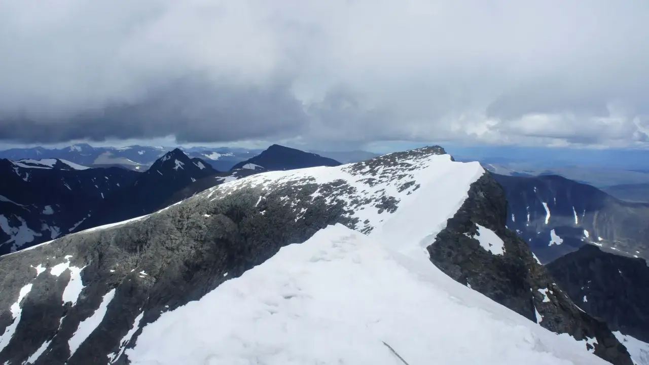 Snöklädda bergstoppar och molniga himlar. En repstump syns i förgrunden, redo för äventyret på Kebnekaise leder.