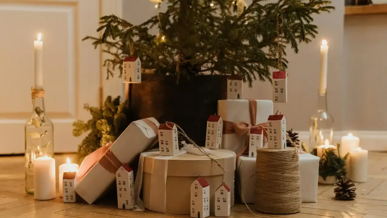 Julkalender tips: En julgran med små hus som dekorationer, presenter och ljus skapar en mysig julstämning.