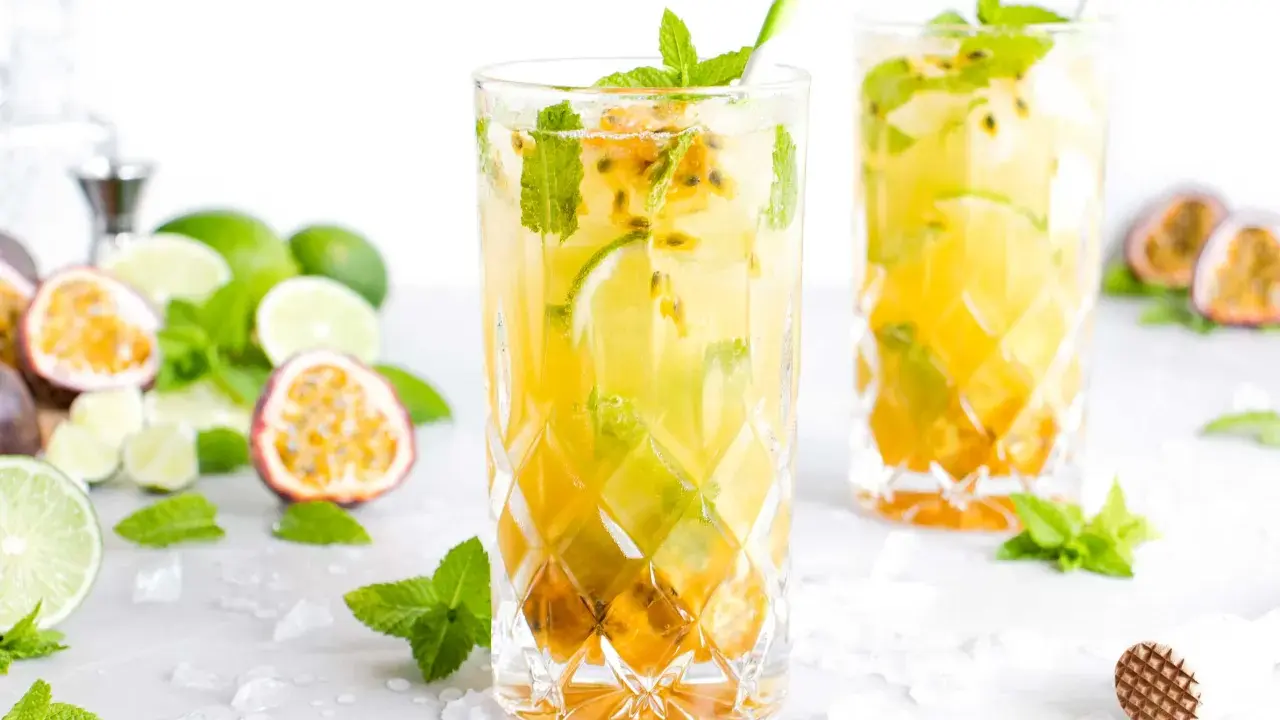 Zwei erfrischende Passion Fruit Mojitos mit Minze und Limette, umgeben von frischen Früchten und Eis.