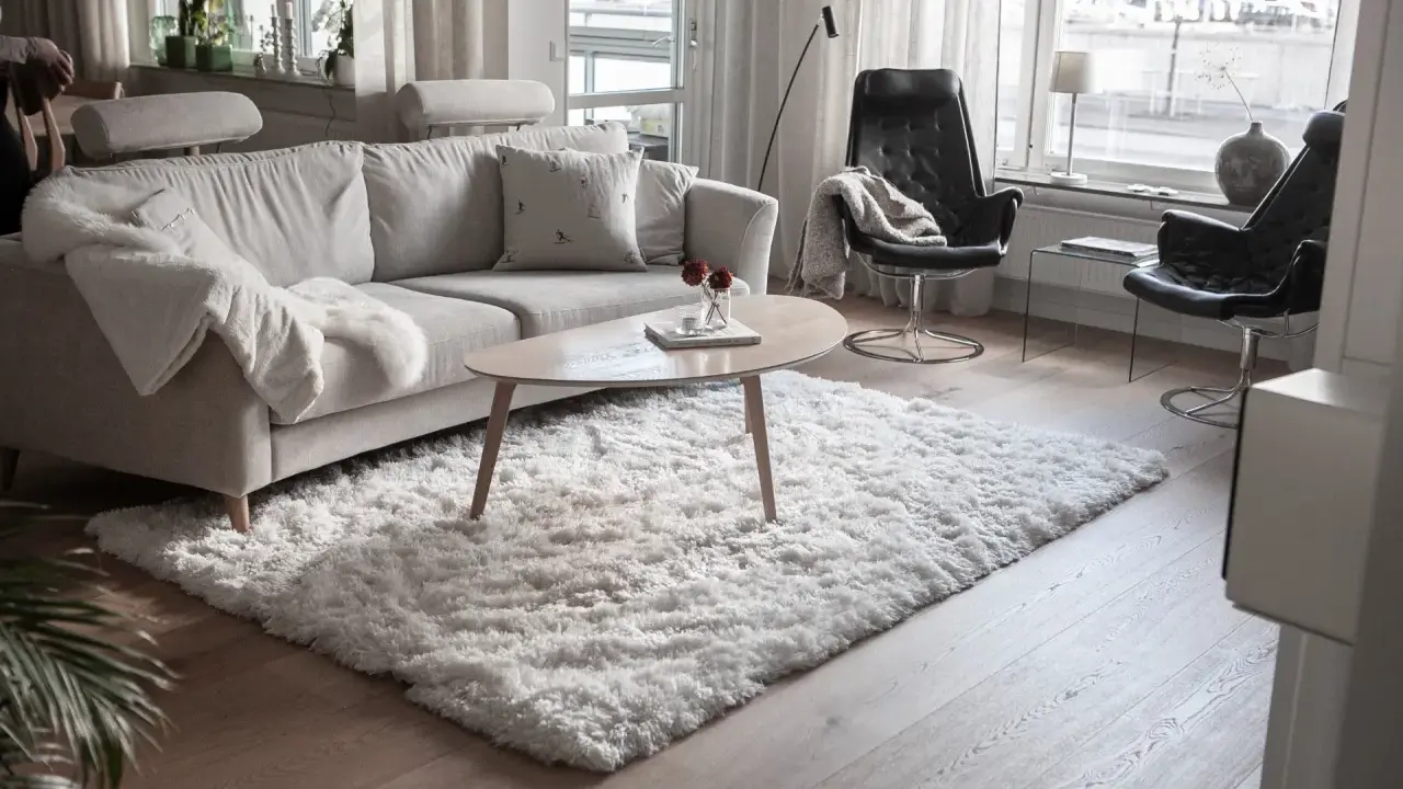 En fluffig, vit matta ligger framför en ljusgrå soffa och skapar en mysig känsla i vardagsrummet.