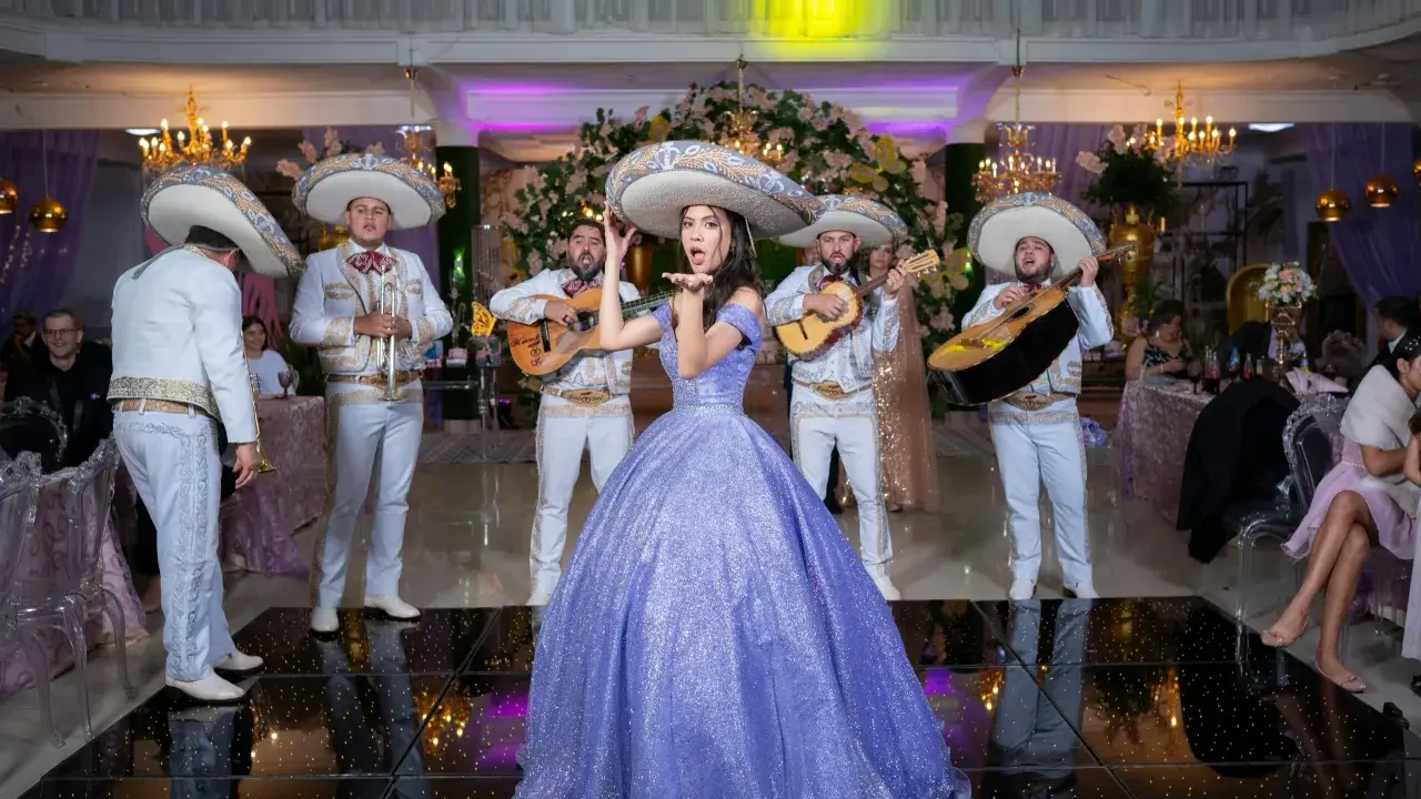 Dziewczyna w fioletowej sukni i mariachi śpiewają, tworząc atmosferę pełną radości i być może sprośnych przyśpiewek.