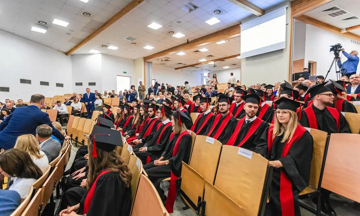 Absolwenci w togach siedzą na uroczystości w sali wykładowej. To ważny dzień dla studentów z Radomia.