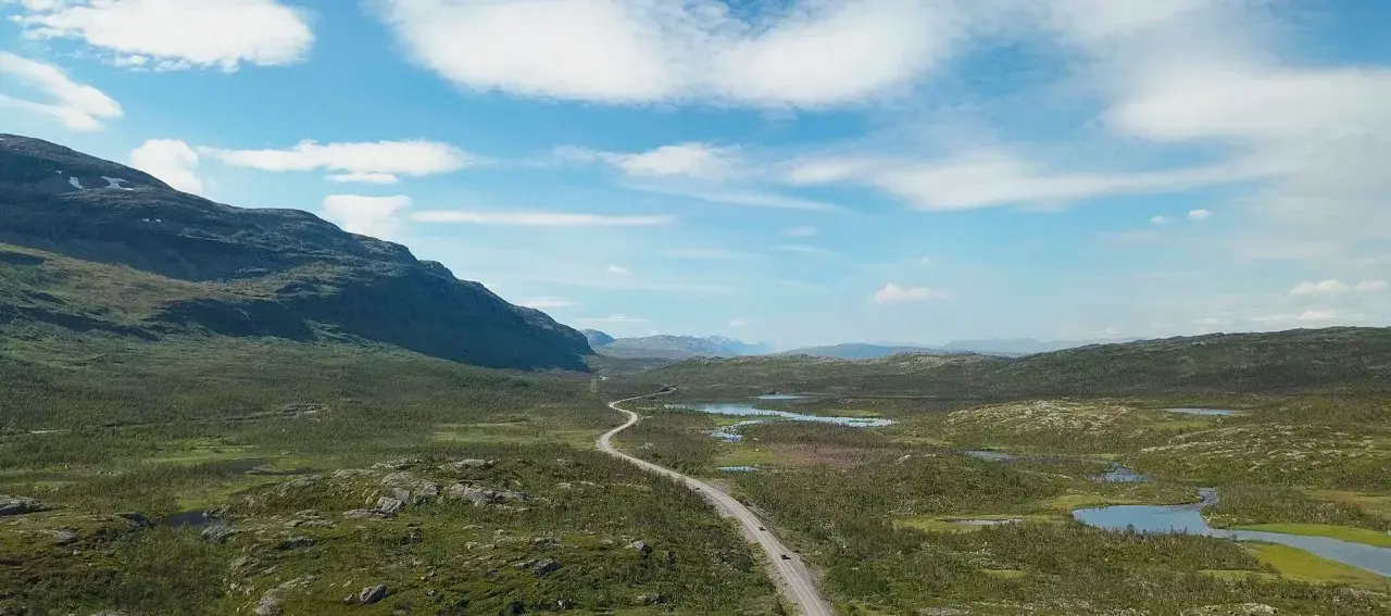 Väg slingrar sig genom ett vidsträckt landskap med berg och sjöar. Perfekt för camping i Norrbotten.