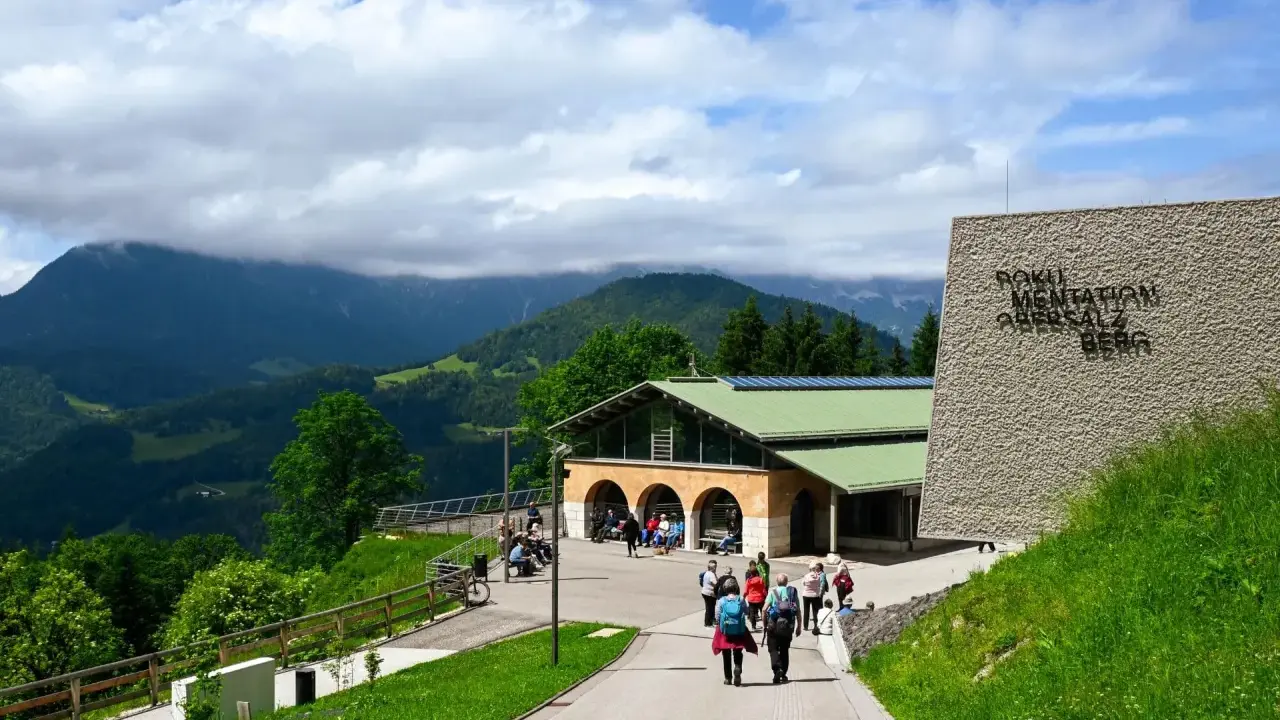 Besucher erkunden das Dokumentationszentrum Obersalzberg, umgeben von grünen Hügeln und Bergen.