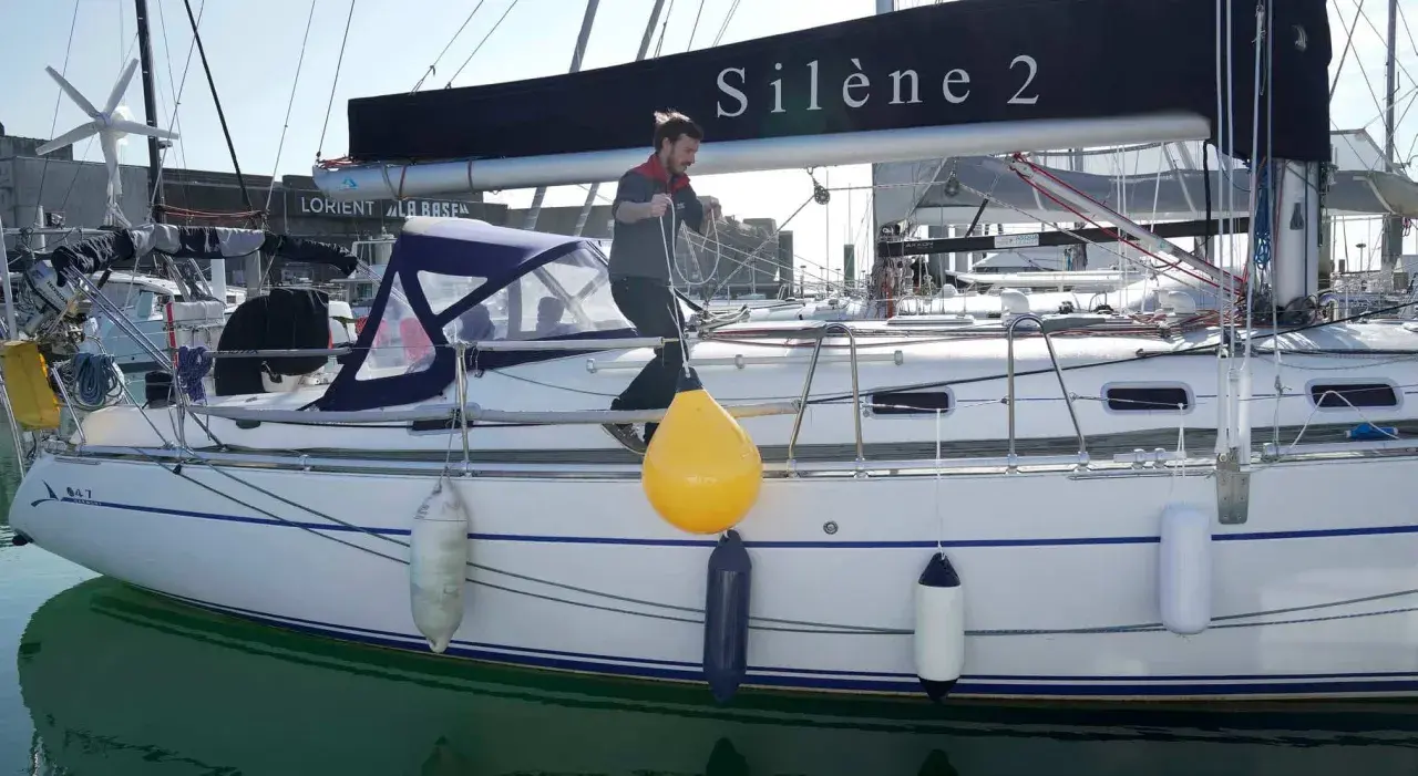 Un homme ajuste un pare-battage jaune sur un voilier. Ces bouées protègent la coque des chocs.