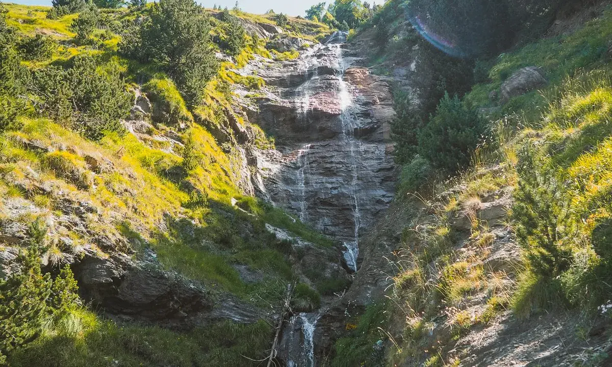 Cascada cayendo por una ladera rocosa, rodeada de vegetación verde y amarilla. Un hermoso paisaje que invita a recorrer la ruta de las tres cascadas.