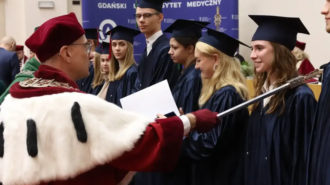 Uroczystość wręczenia dyplomów na studiach w Trójmieście. Absolwenci w togach odbierają gratulacje.