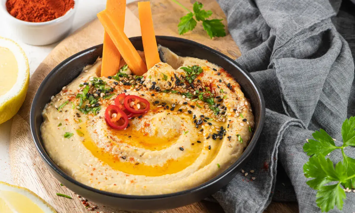 Hummus cremoso con bastones de zanahoria, pimientos rojos y semillas. Un snack saludable ideal para el embarazo.
