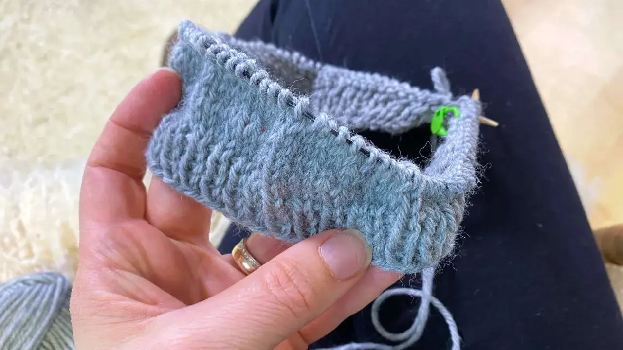 En hand håller ett stickat provstycke i ljusgrått garn. Tekniken german short rows används för att forma det.