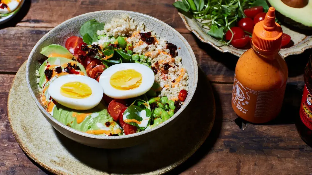 Gesunde Bowl-Ideen: Quinoa, Avocado, Ei, Edamame und Kirschtomaten, beträufelt mit Sriracha-Mayo.