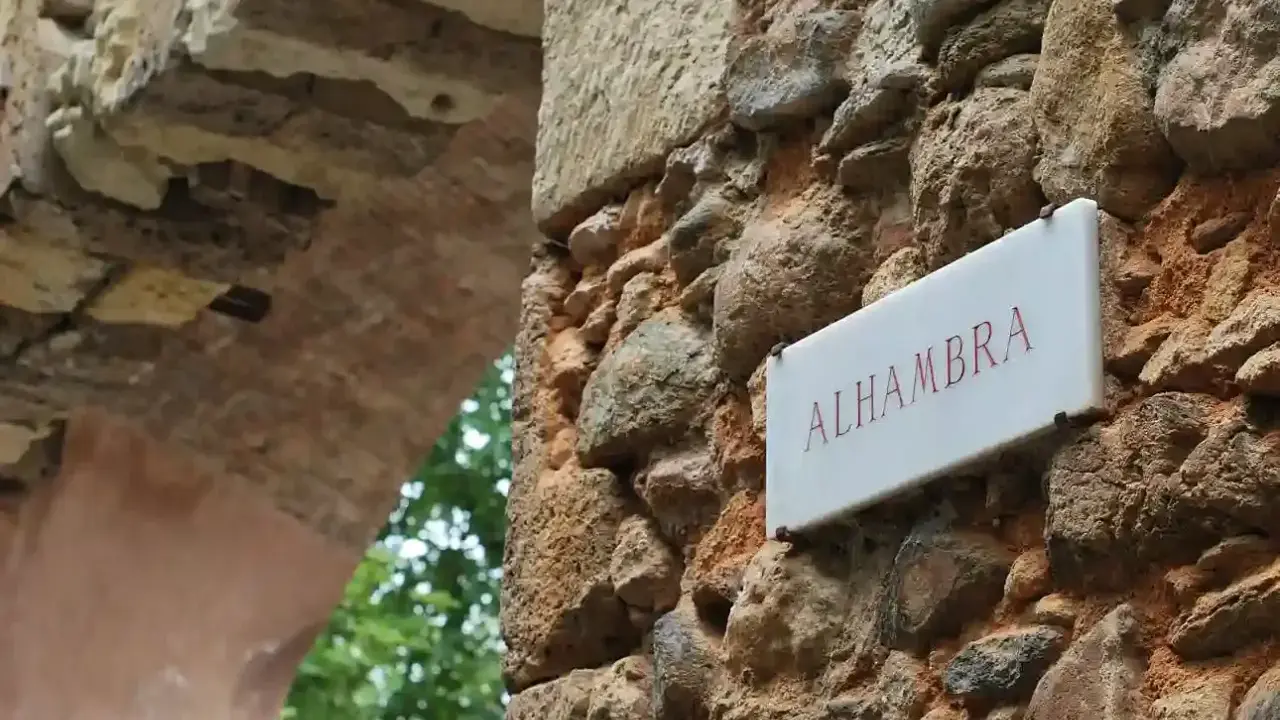 Schild "Alhambra" an einer alten Steinmauer, die zu einem Parkplatz führt.