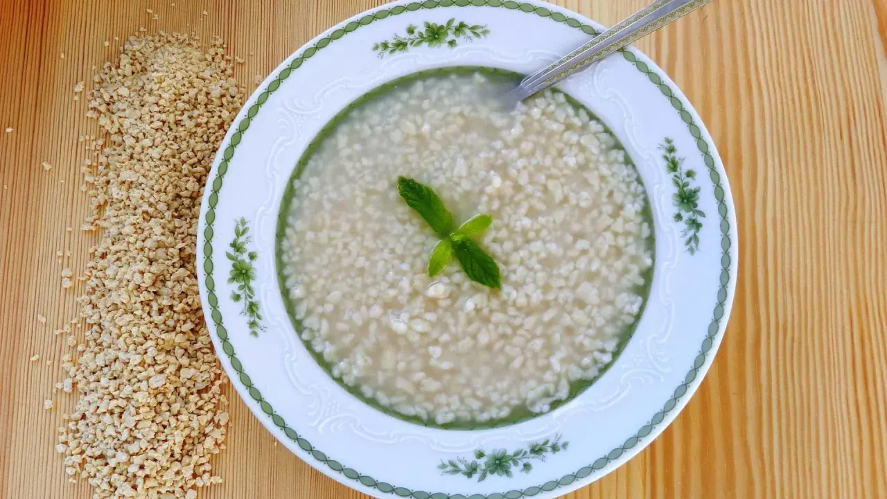 Eine Schüssel mit Trahana, garniert mit Minze, neben einem Haufen getrockneter Trahana. Ein Löffel liegt in der Schüssel.