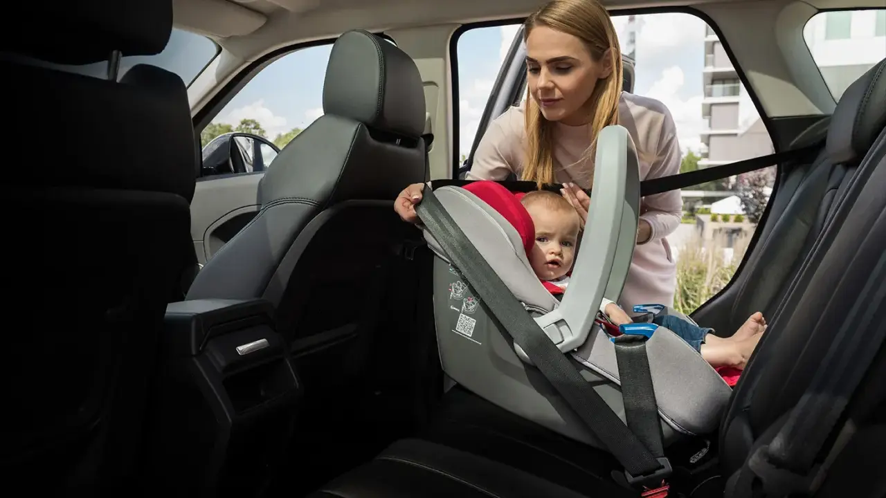 Mama pokazuje, jak zapiąć fotelik pasem, by bezpiecznie przewieźć malucha.