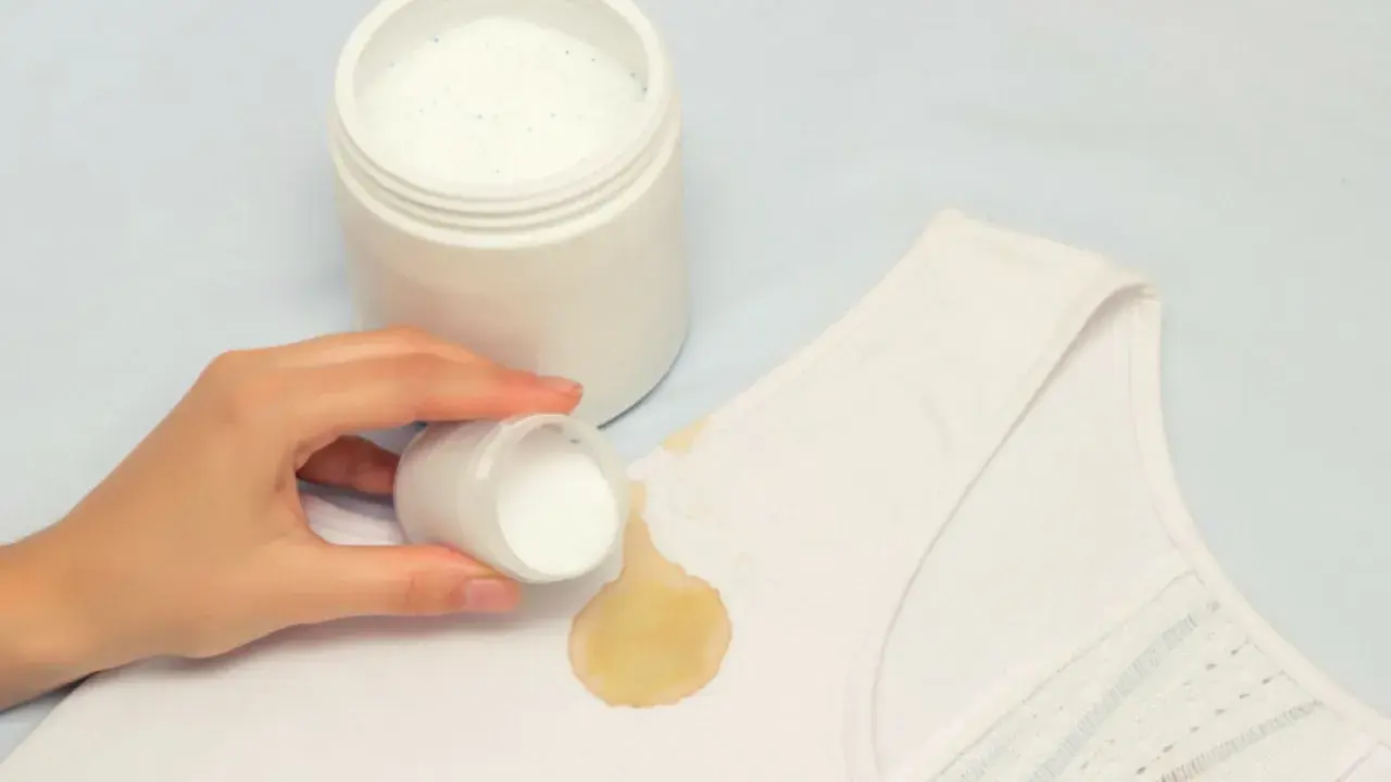 Mano aplica polvo blanqueador sobre mancha amarilla en ropa blanca. ¡Descubre cómo blanquear ropa blanca fácilmente!