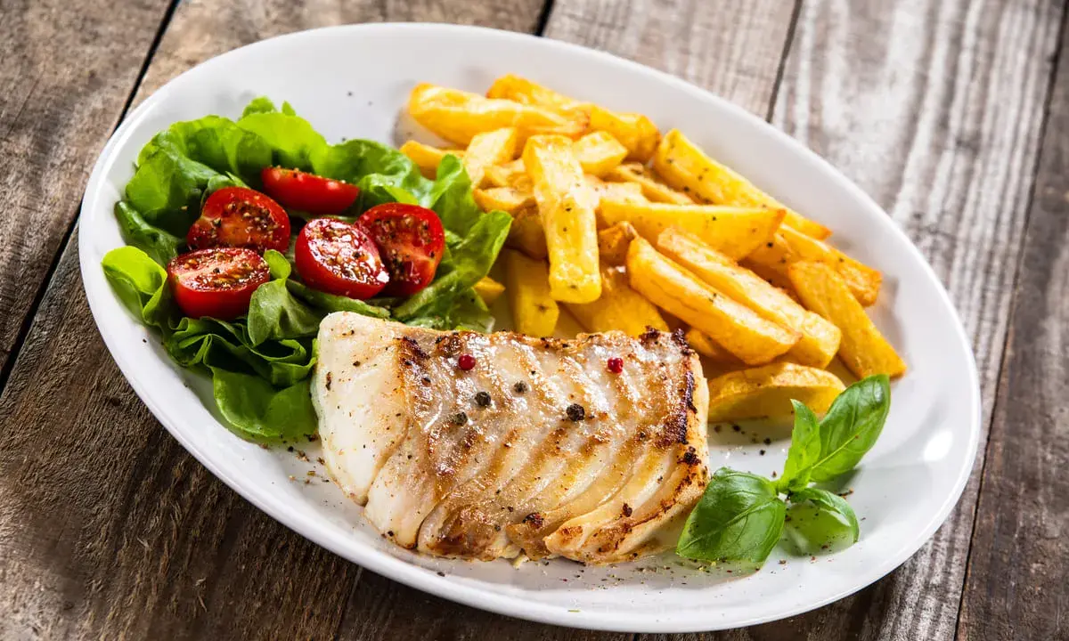 Idealne jakie przyprawy do ryby? Pieprz i sól na grillowanym filecie, obok frytki i sałatka z pomidorkami.