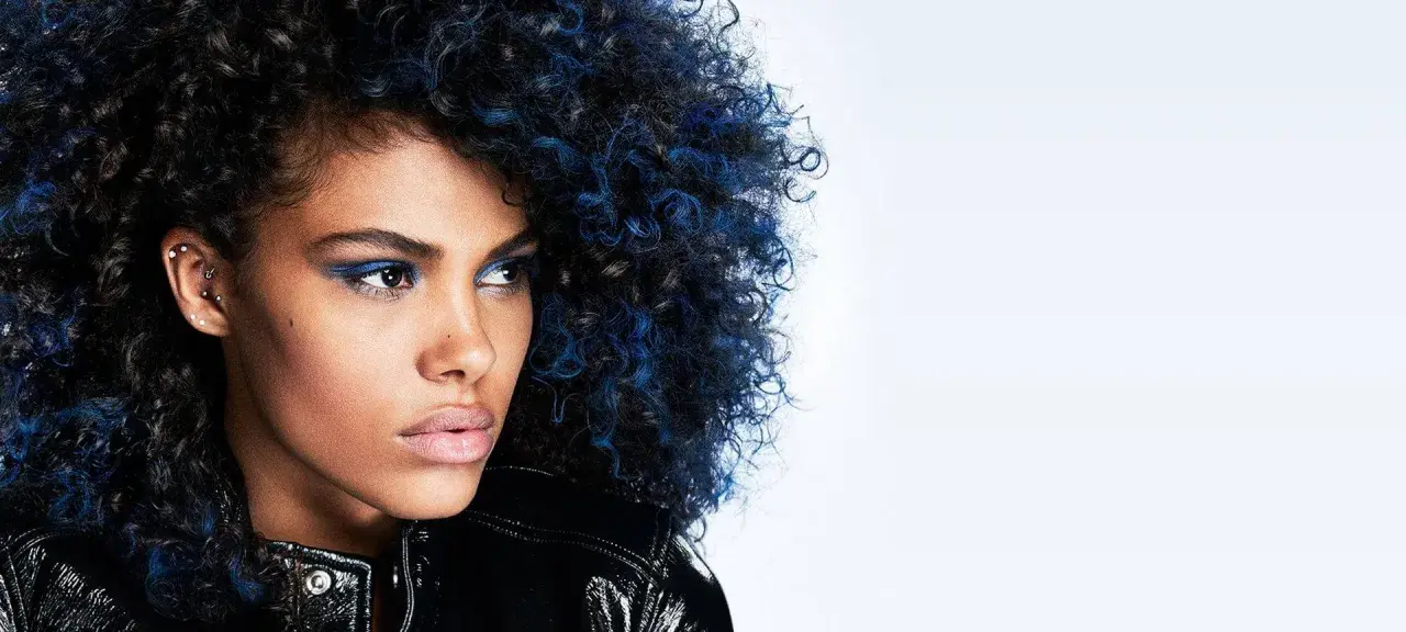 Mujer con cabello rizado negro azulado y maquillaje vibrante, luciendo una chaqueta brillante.