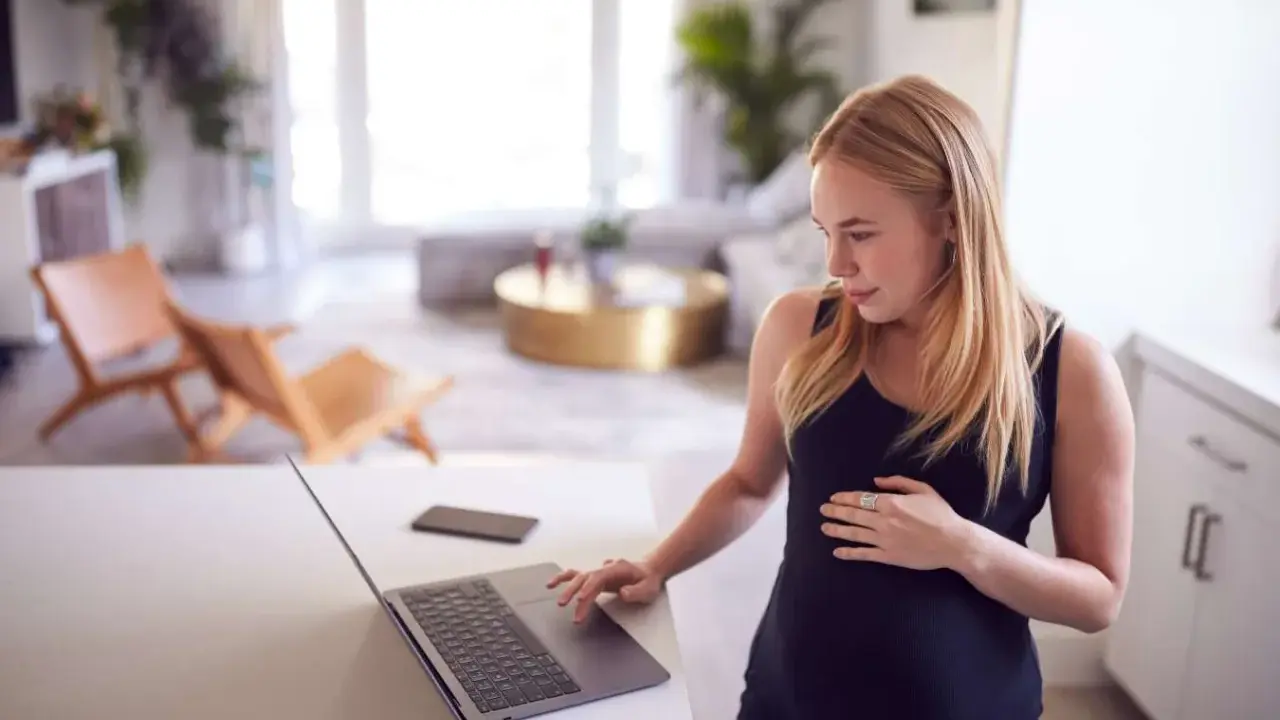 Ciężarna kobieta sprawdza na laptopie, czy skurcze co 20 minut oznaczają poród.