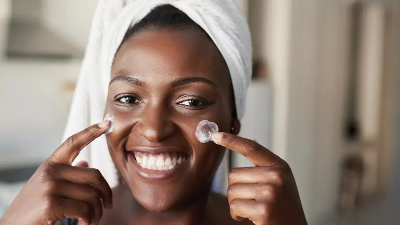 Sourire radieux, une femme applique une crème sur ses joues. Un avant-après prometteur pour une peau éclatante grâce au rétinol.