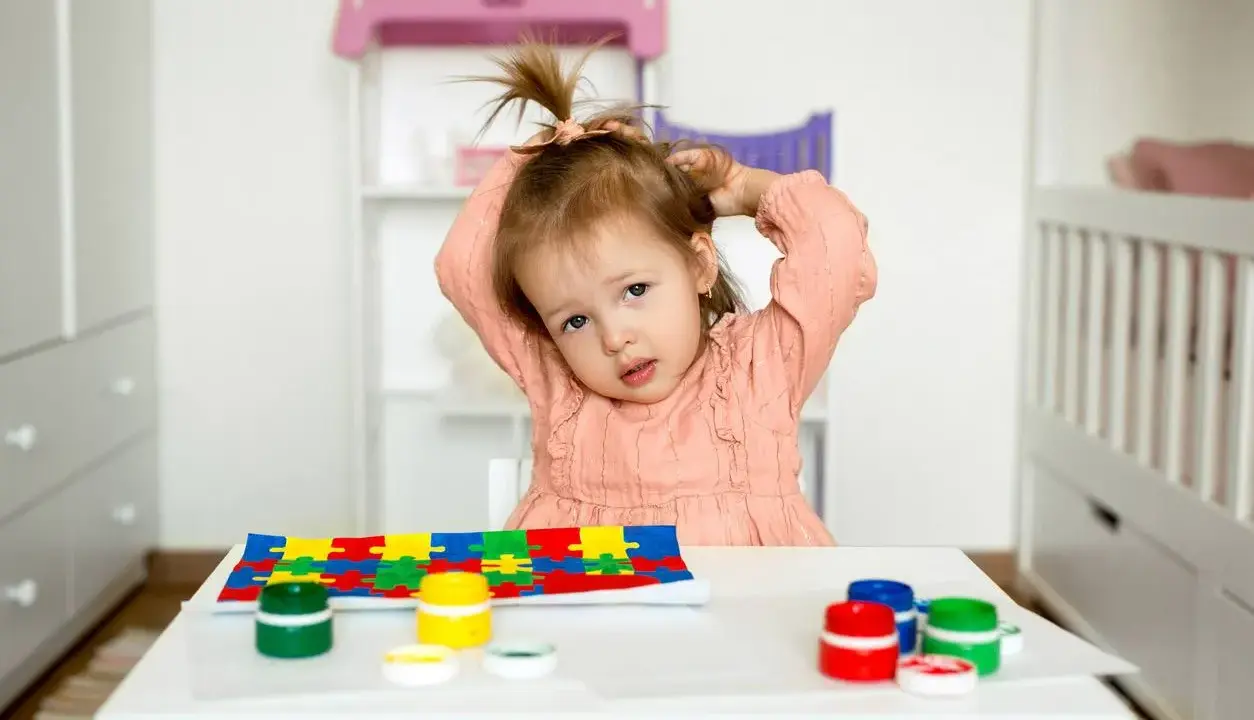 Bambina con puzzle e colori, un'immagine che fa riflettere su cos'è l'asperger e come supportare i bambini.
