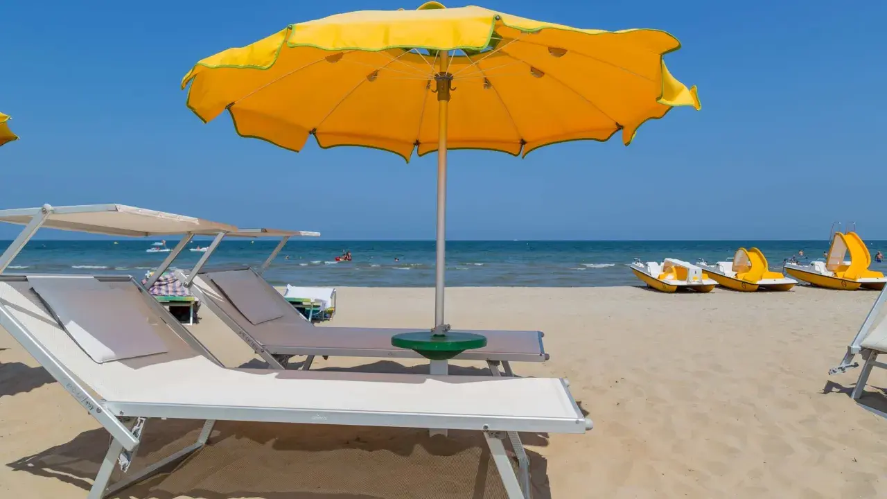 Spiaggia con lettini e ombrellone giallo, pedalò in attesa, mare calmo e cielo azzurro, tipico di tanti paesi vicino Rimini sul mare.