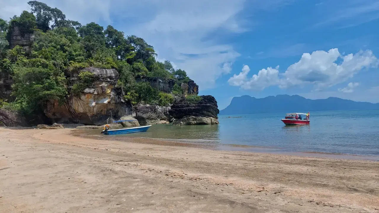 Spiaggia in Malesia con bambini su una barca rossa. Rocce verdi e mare azzurro.