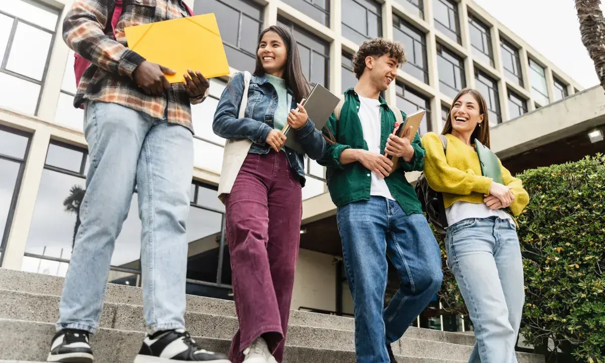 Studenci idą po schodach, rozmawiając i śmiejąc się. Czy ich wysoka średnia pozwoli im zdobyć stypendium?