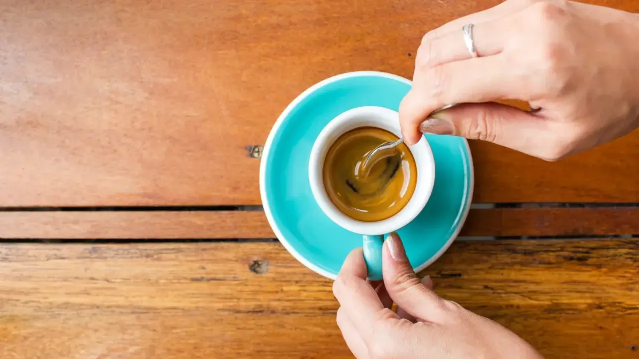 Mani che mescolano un caffè, nonostante si dica che il caffè è cancerogeno, il suo aroma attira.