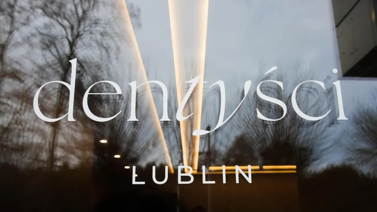 Napis "Dentyści Lublin" na szklanych drzwiach z odbiciem drzew i światła.