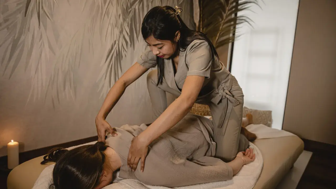 Relaksacyjny shiatsu masaż pleców. Terapeuta klęczy obok klienta leżącego na macie, wykonując delikatne naciski.