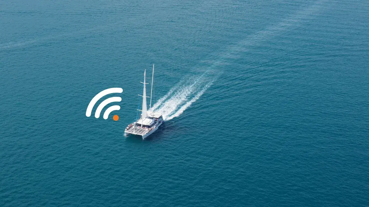 Un catamaran à voile navigue sur une mer bleue, avec un symbole de connexion Wi-Fi à proximité.