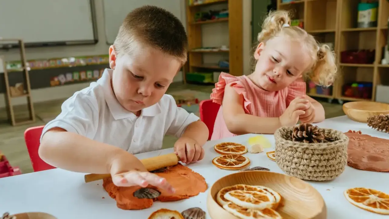 Niños de 3 a 4 años disfrutan de actividades creativas en casa, moldeando arcilla y decorando con elementos naturales.