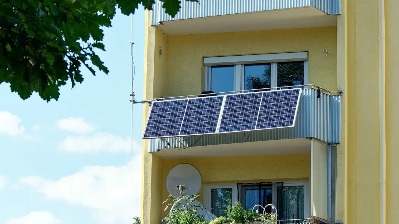 Två solceller monterade på en balkong på ett gult flerfamiljshus. Gröna växter i krukor på den nedre balkongen.