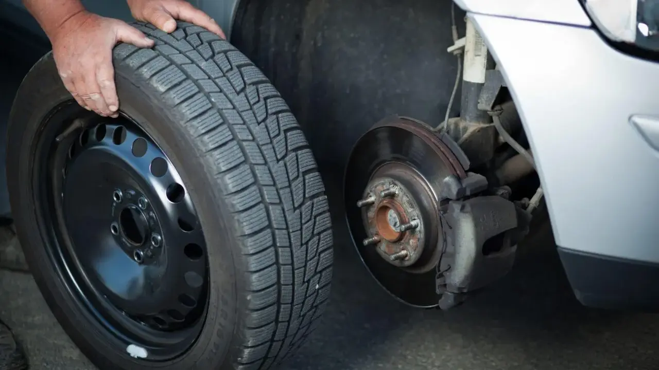 Mani che cambiano una gomma invernale, rispettando l'obbligo cambio gomme per la sicurezza stradale.