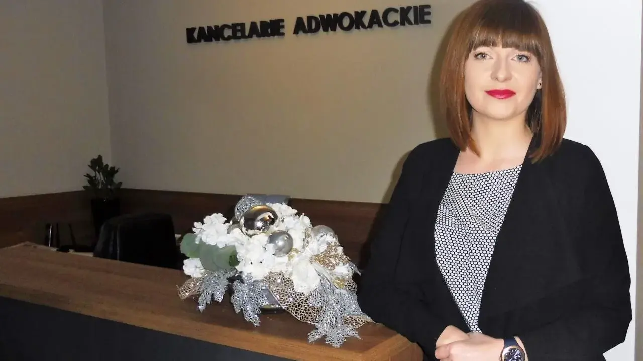 Kobieta w czarnym żakiecie przy recepcji z dekoracją kwiatową. Napis "KANCELARIE ADWOKACKIE".
