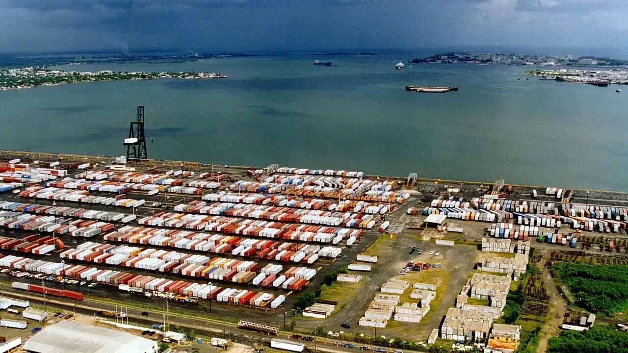 Vasto deposito di container nel porto di San Juan, Porto Rico, con navi in lontananza sotto un cielo nuvoloso.