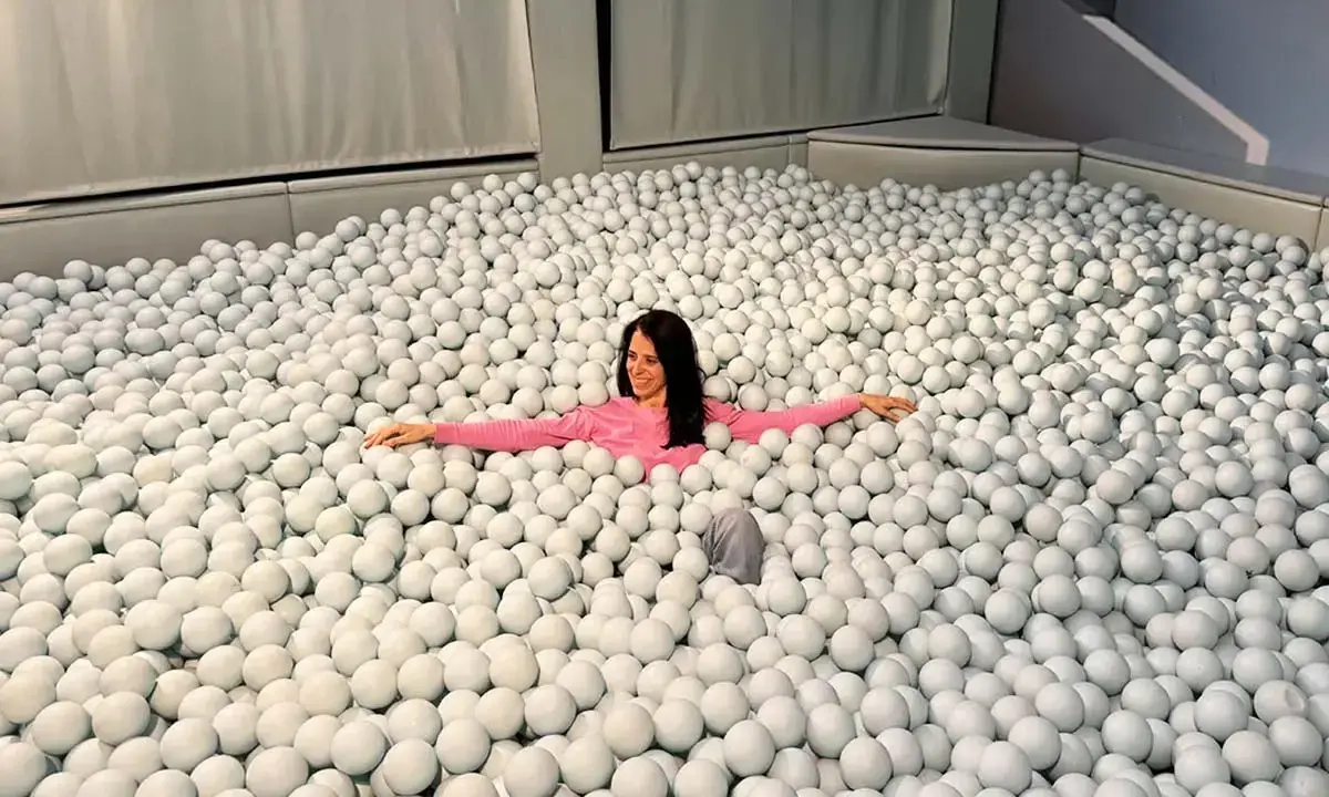 Mujer sonriente se sumerge en una piscina de bolas blancas, un divertido ikono madrid.