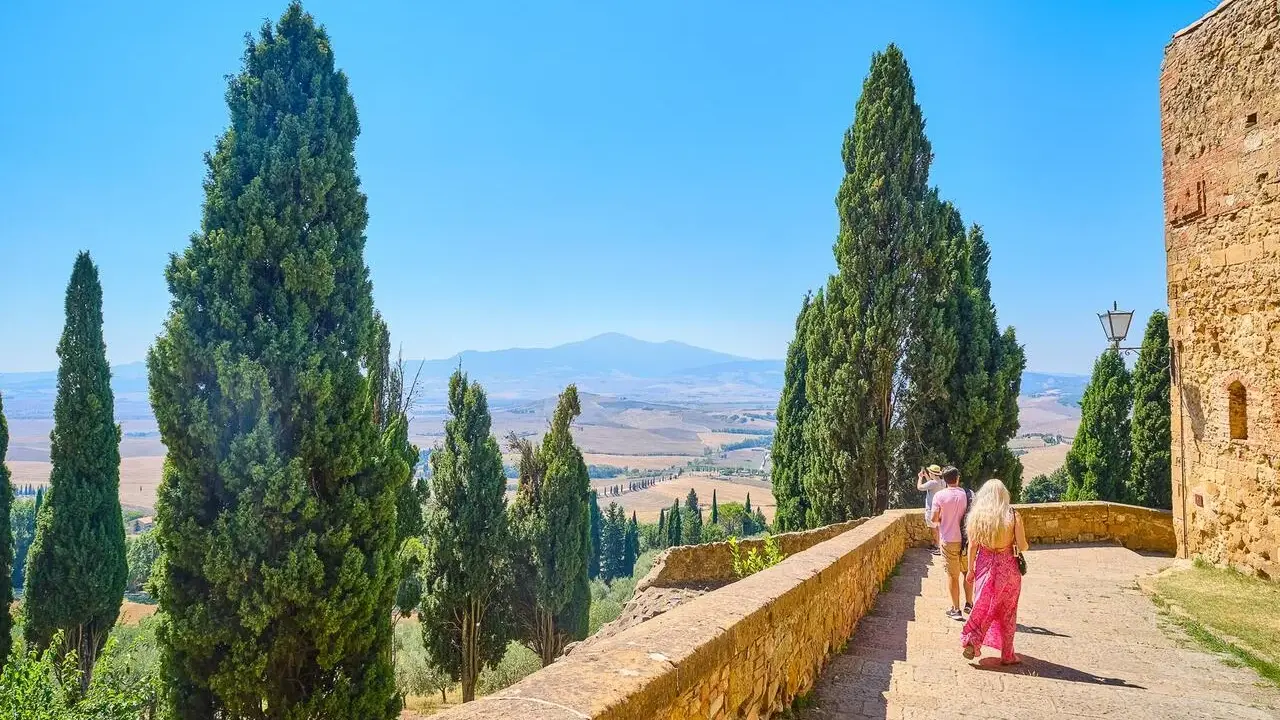 Coppia in cammino durante un tour Toscana 5 giorni, tra cipressi e colline ondulate sotto un cielo azzurro.