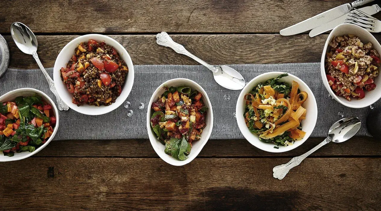 Verschiedene Salate als Beilagen für ein Fondue: Linsensalat, Gemüsesalat mit Karotten und Grünkohl, sowie ein weiterer bunter Salat.