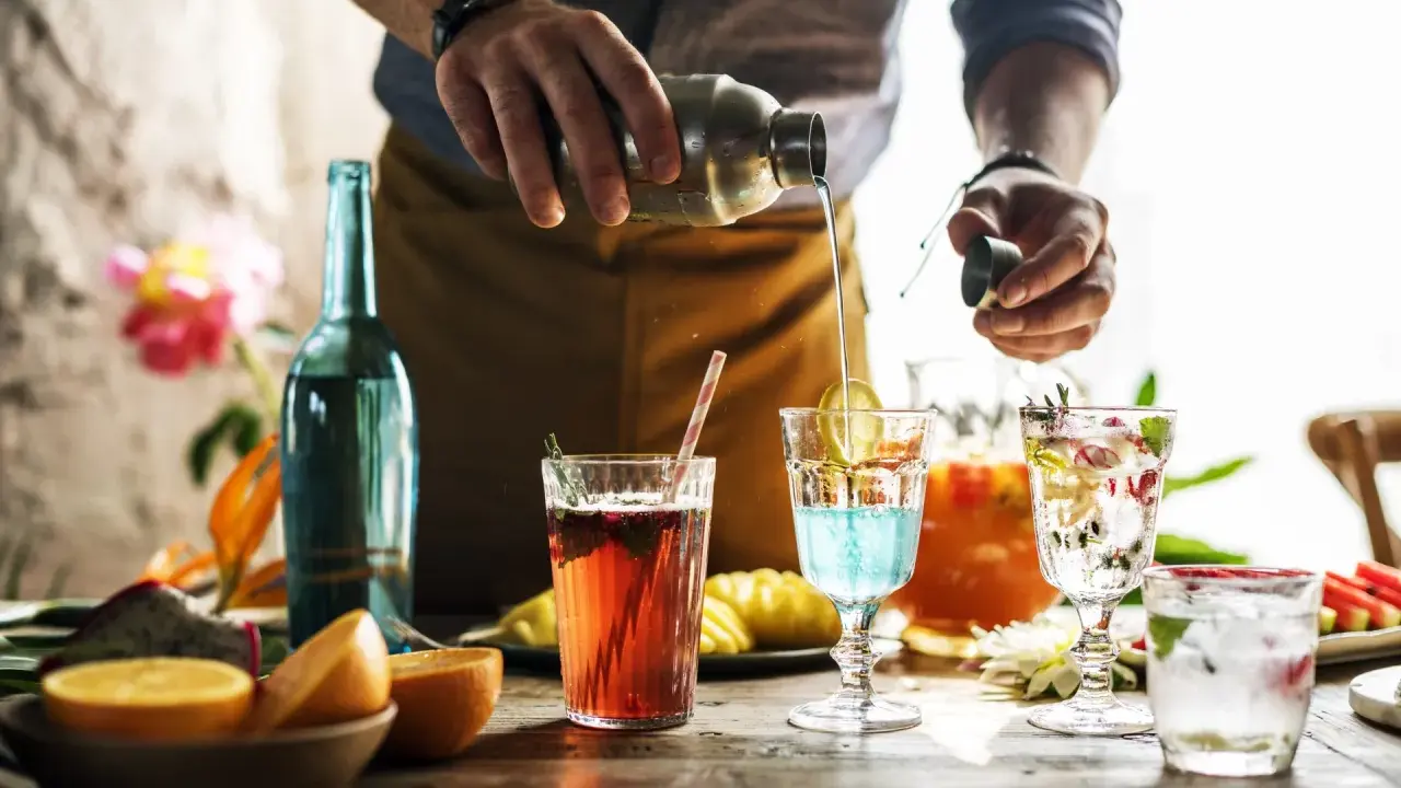 Barman przelewa płyn z shakera do drinka, tworząc kolorowe koktajle. Mieszanie alkoholi to sztuka.